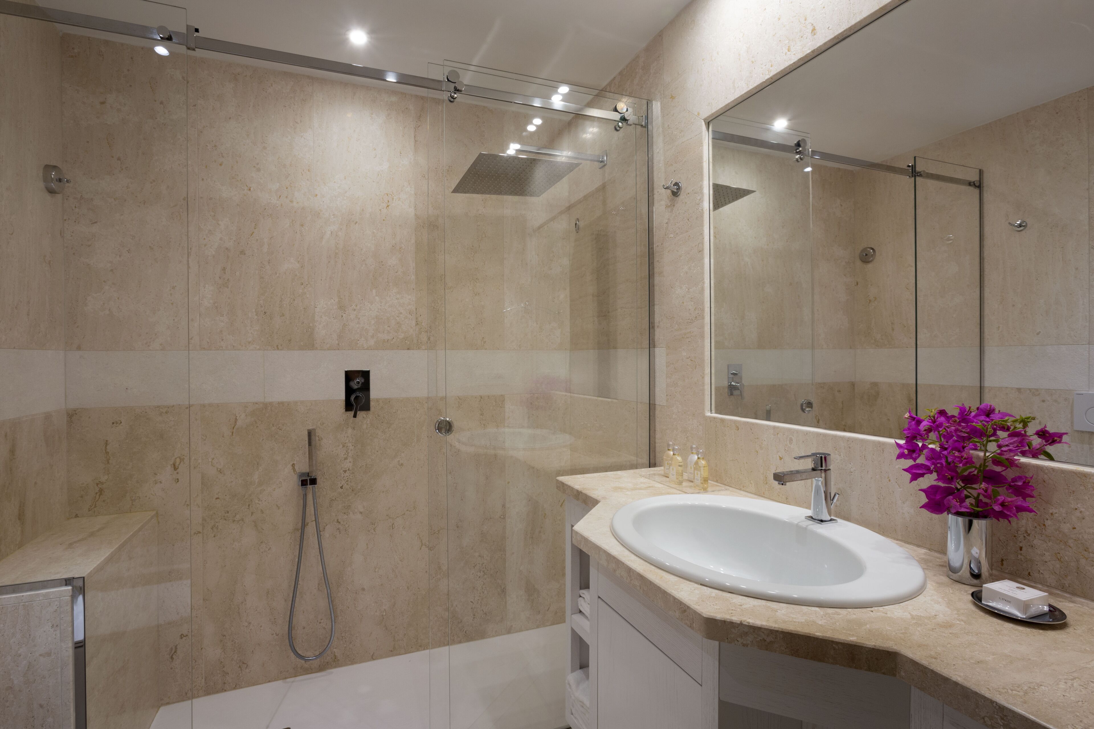 A modern bathroom with a glass-enclosed shower, a white sink, and a large mirror.