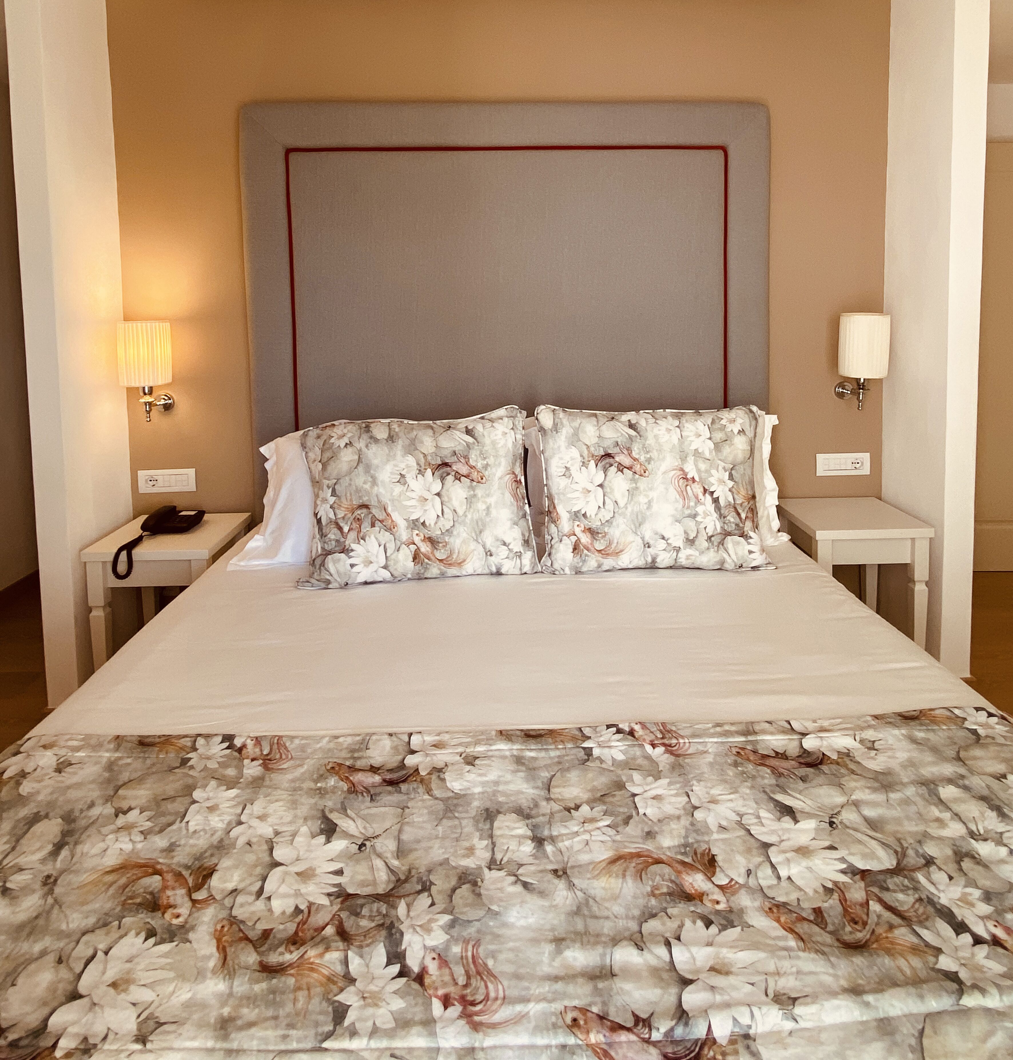 A hotel room with a bed, two nightstands, a lamp on each nightstand, and a floral-patterned bedspread.