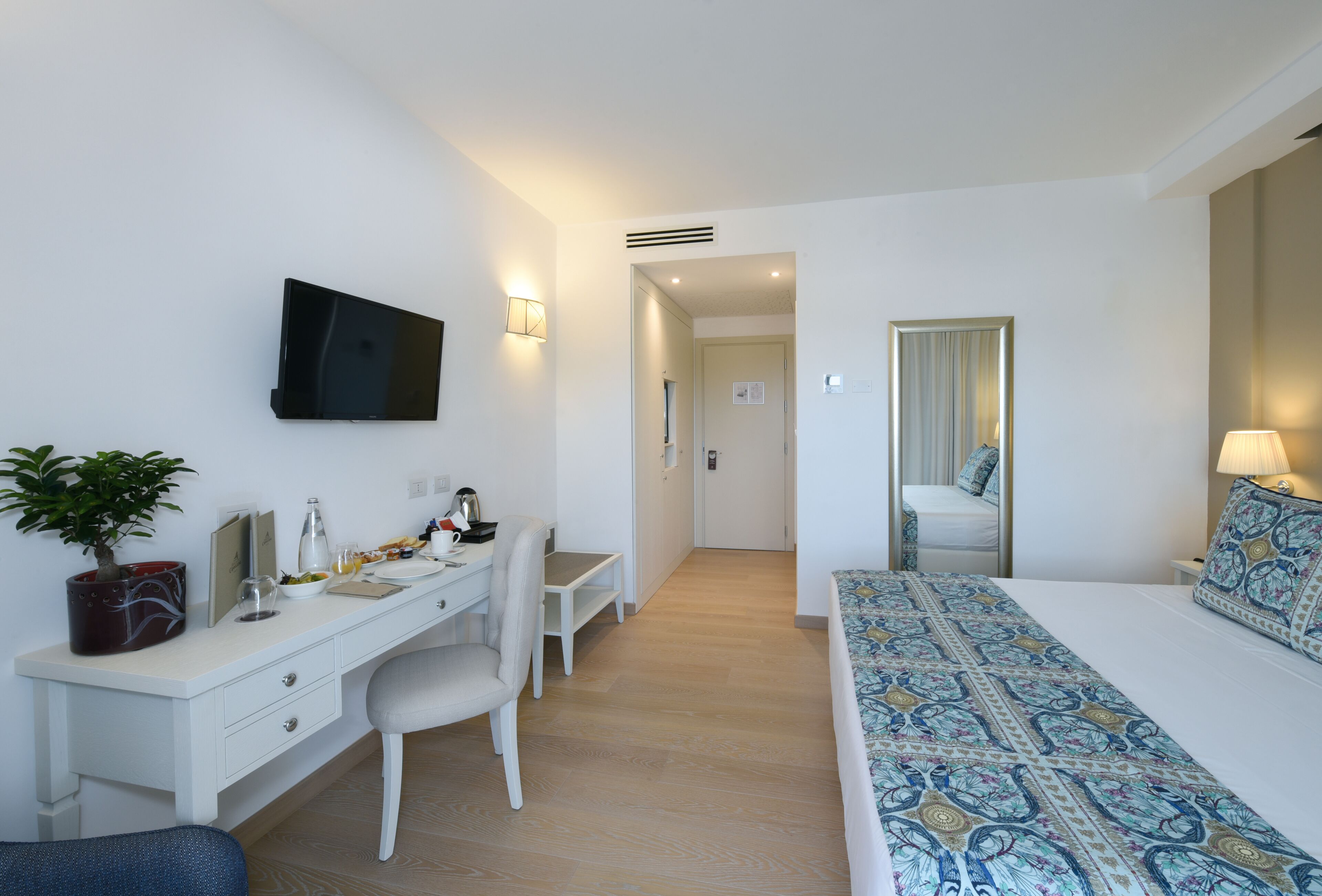 Une chambre d’hôtel équipée d’un lit, d’un bureau, d’une chaise et d’un téléviseur fixé au mur.