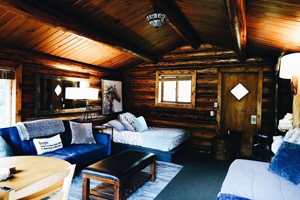 A cozy log cabin interior with a wooden ceiling, a sofa, a bed, and a dining table.
