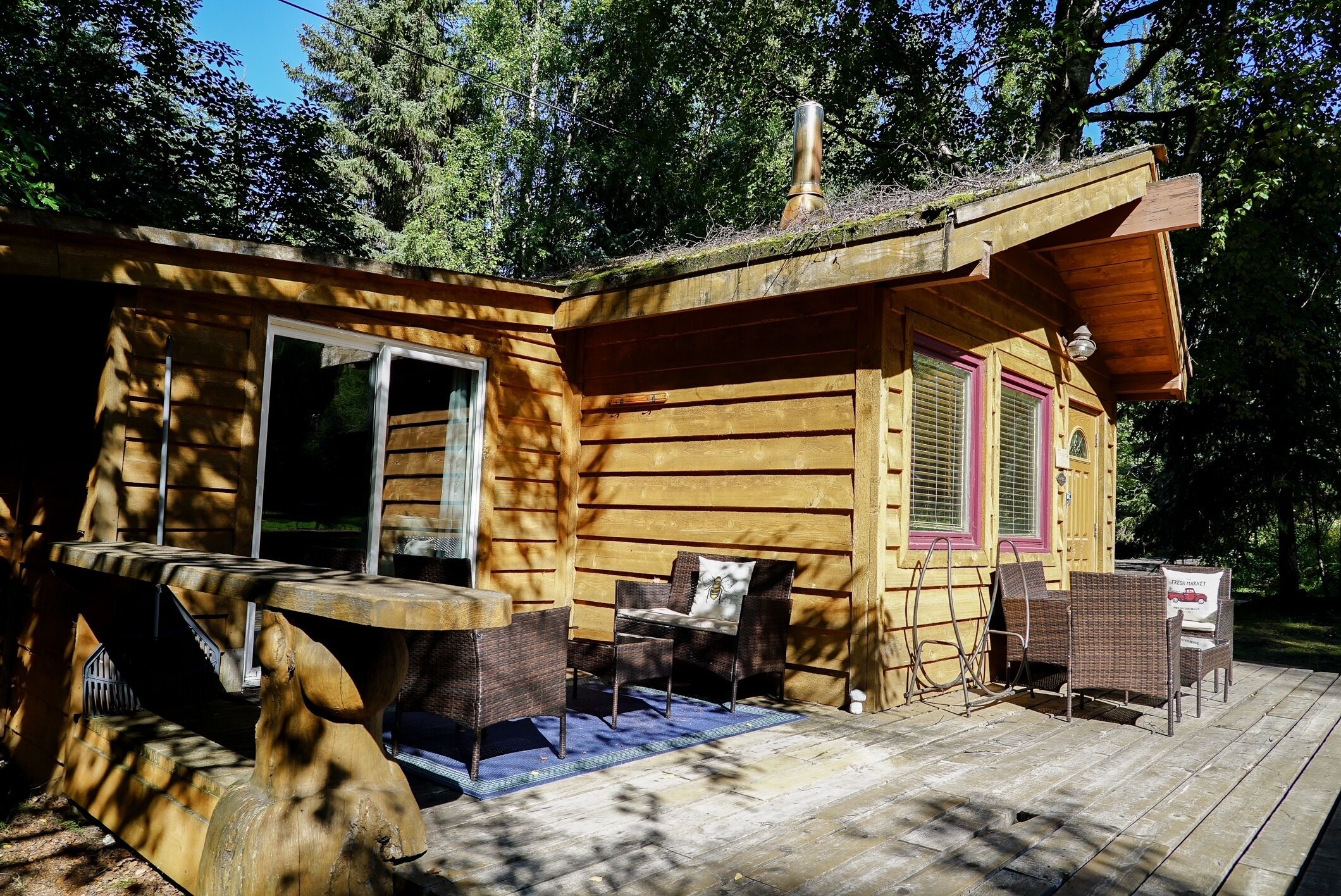 Une cabane en bois dotée d’une terrasse, de meubles en osier et d’une grande fenêtre.