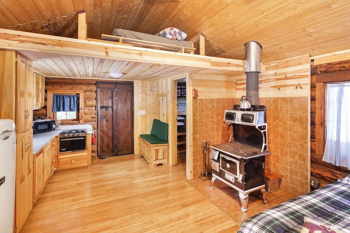 A cozy cabin interior with a kitchen, a dining area, and a sleeping loft.