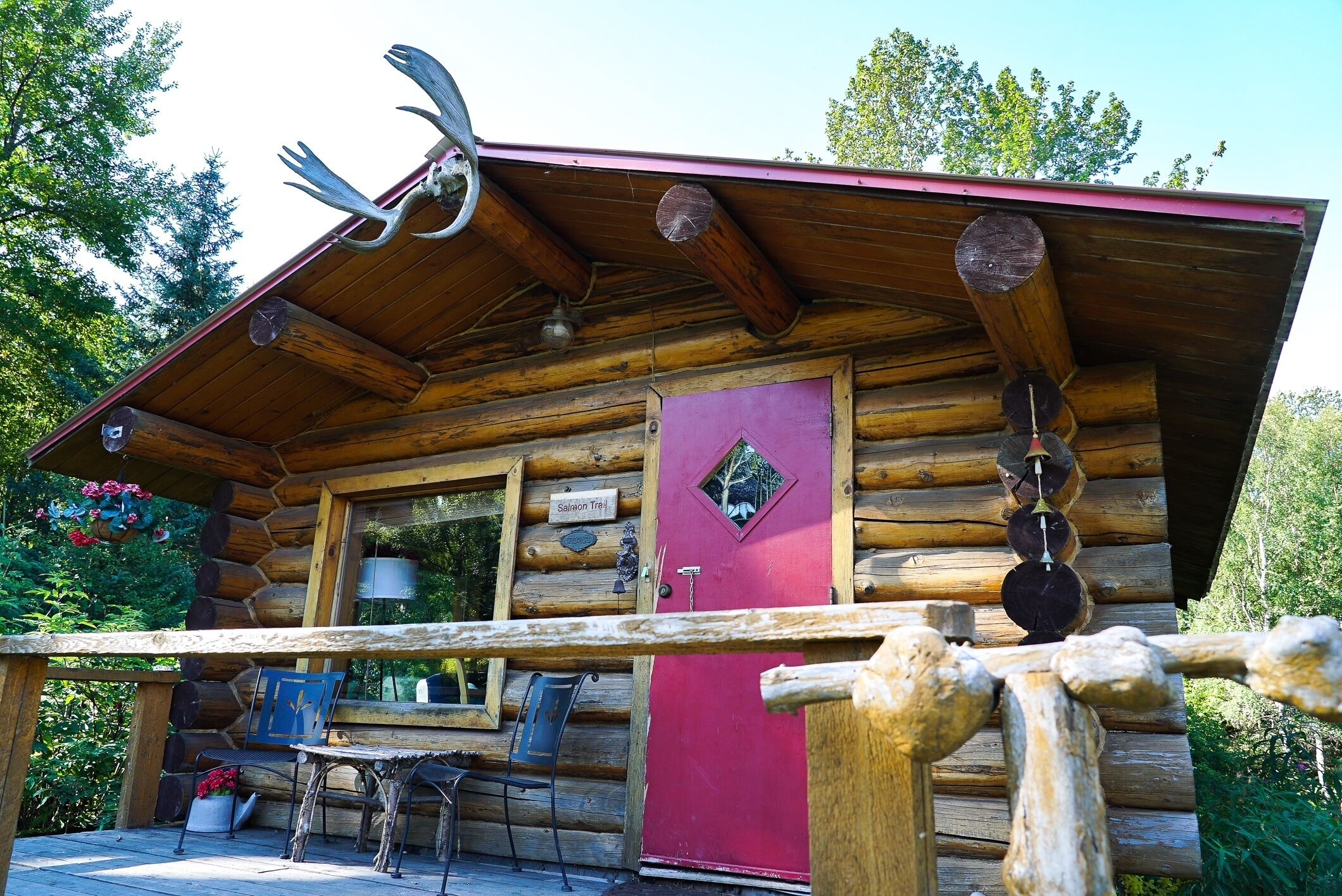 A log cabin with a red door, a wooden porch, and a metal railing.
