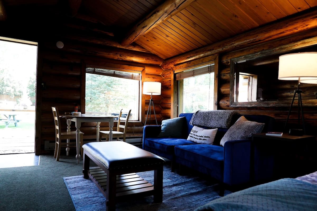 A log cabin interior with a blue sofa, wooden bench, and a dining table with chairs.