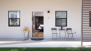 A modern exterior with a door leading to a bedroom, a small seating area with a table and chairs, and a potted plant. - Hotel Flora & Fauna (Wimberley)