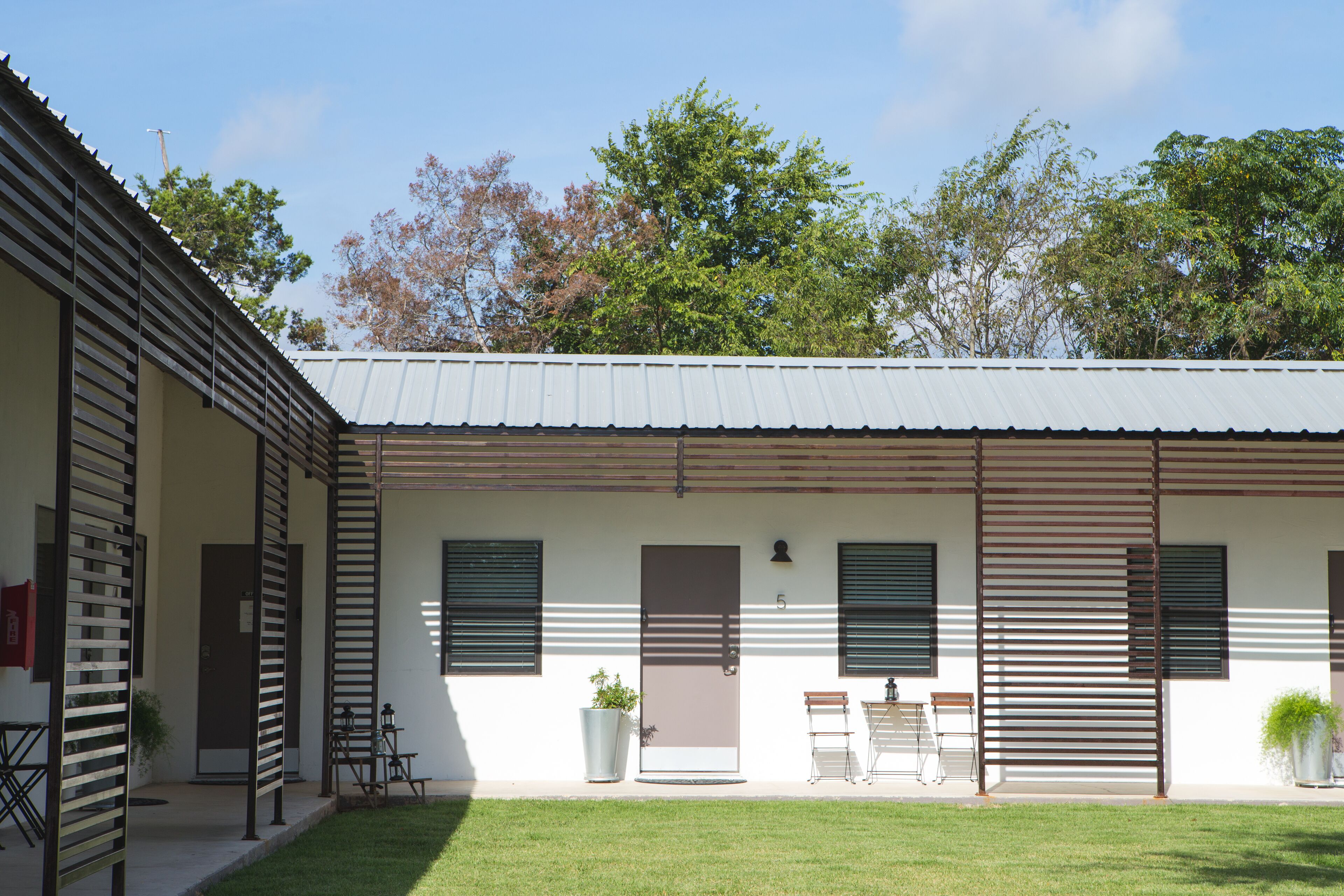A two-story building with a flat roof, a covered patio area, and a small garden.