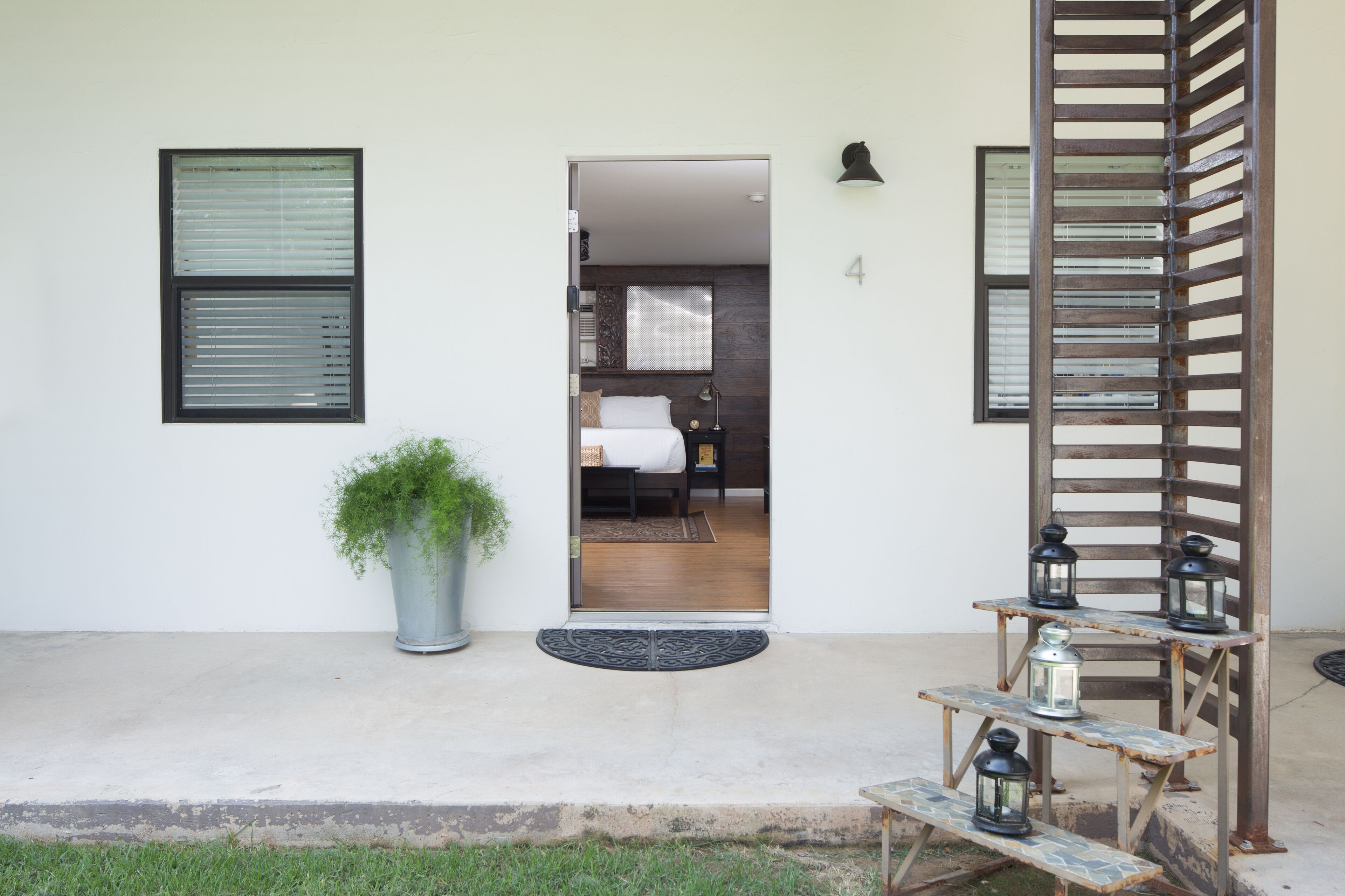 A modern entrance with a concrete floor, a potted plant, a wooden bench, and a metal lantern stand.