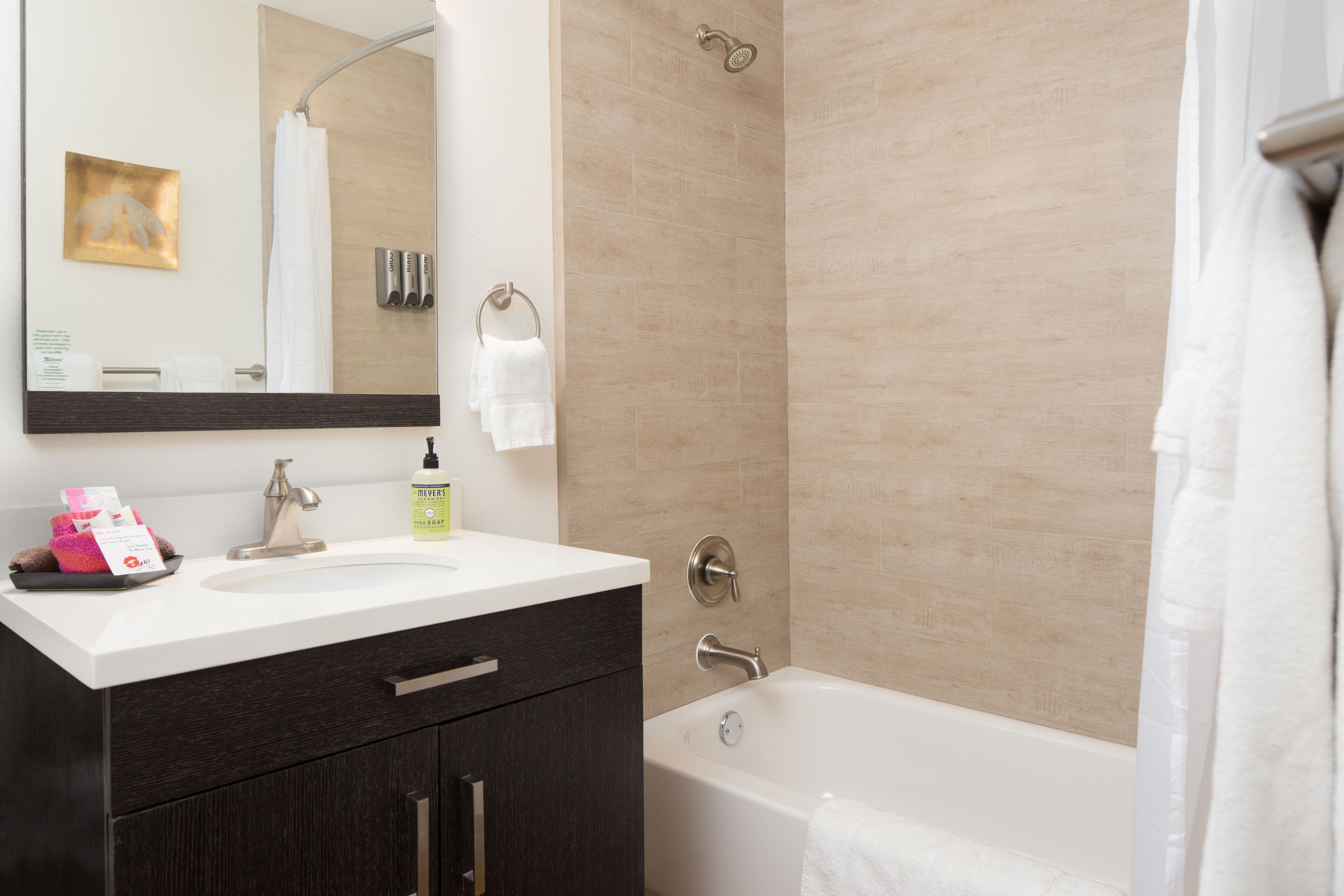 A modern bathroom with a white sink, dark cabinets, a bathtub, and a shower.