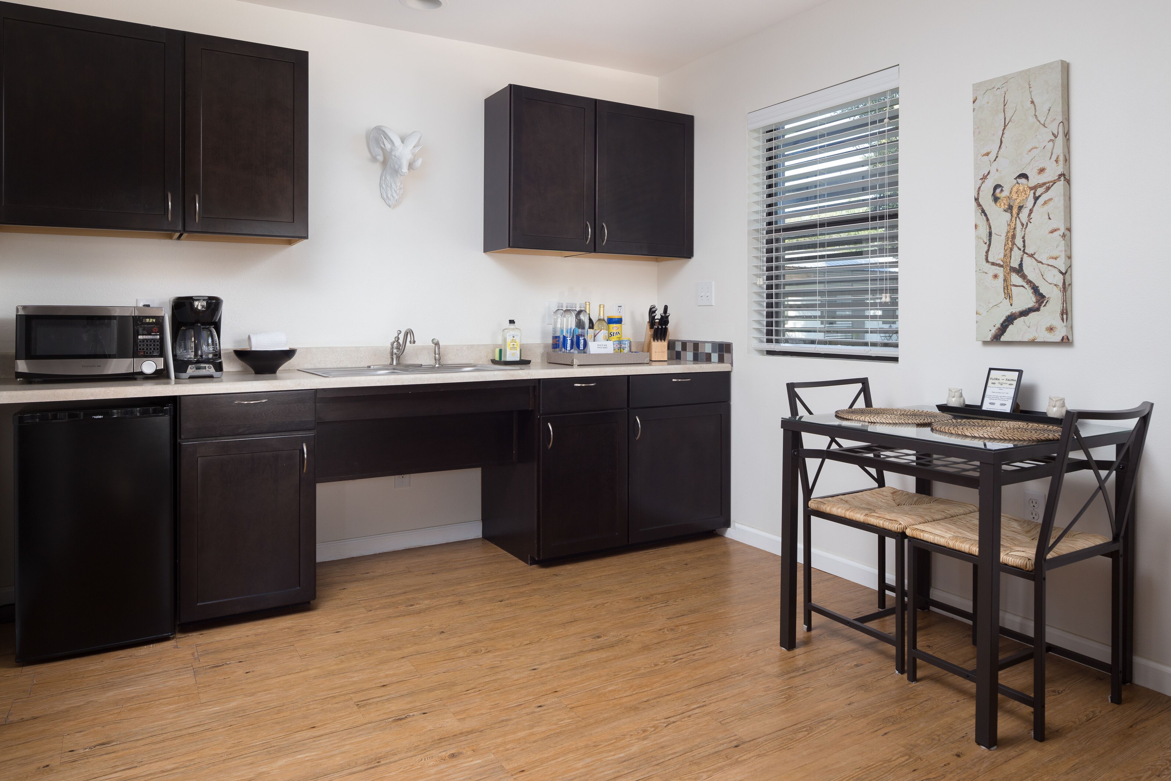 A modern kitchen with dark cabinetry, a microwave, coffee maker, and a dining area with a table and chairs.