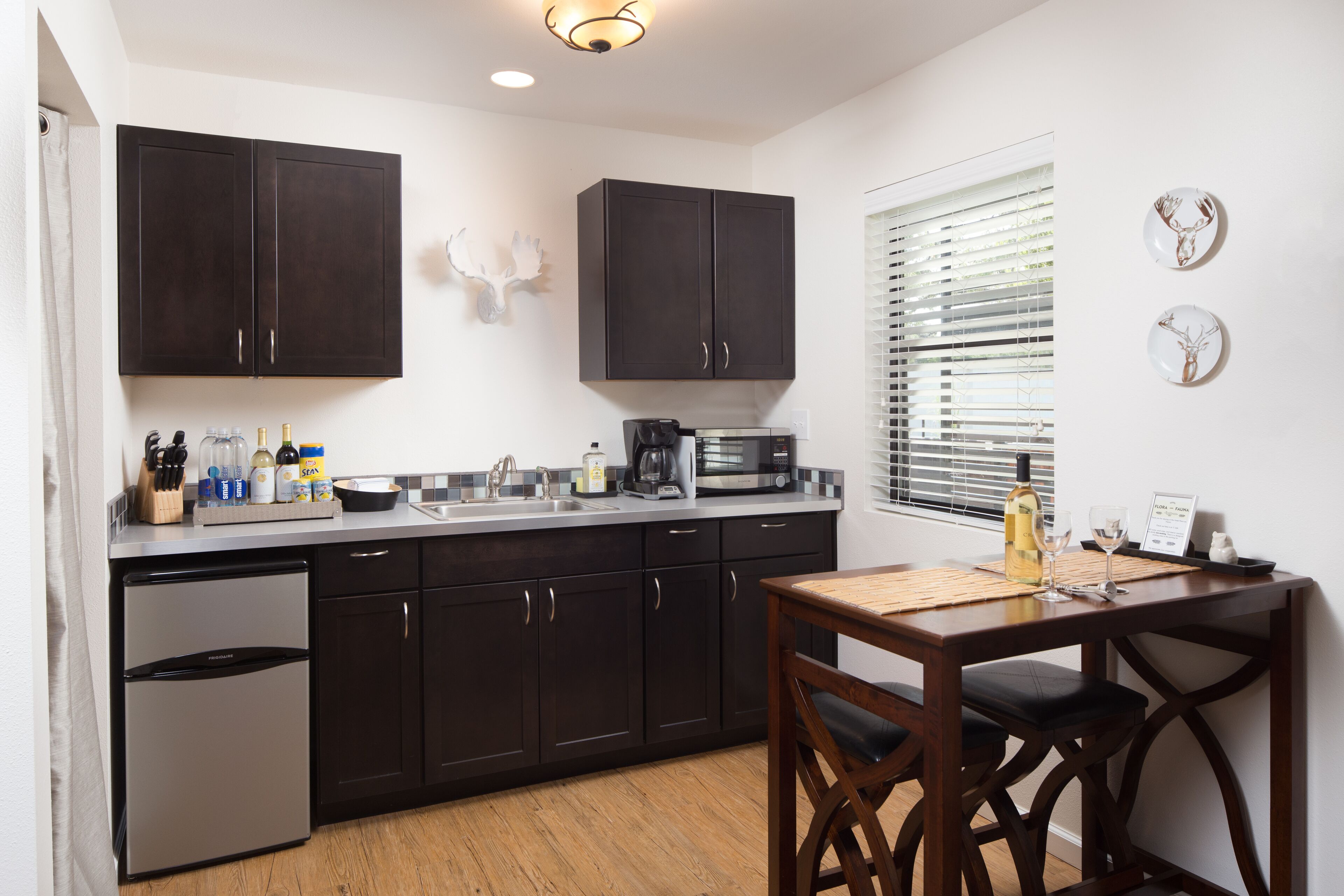 A modern kitchen with dark cabinets, a built-in dishwasher, a microwave, and a dining area with a wooden table and chairs.