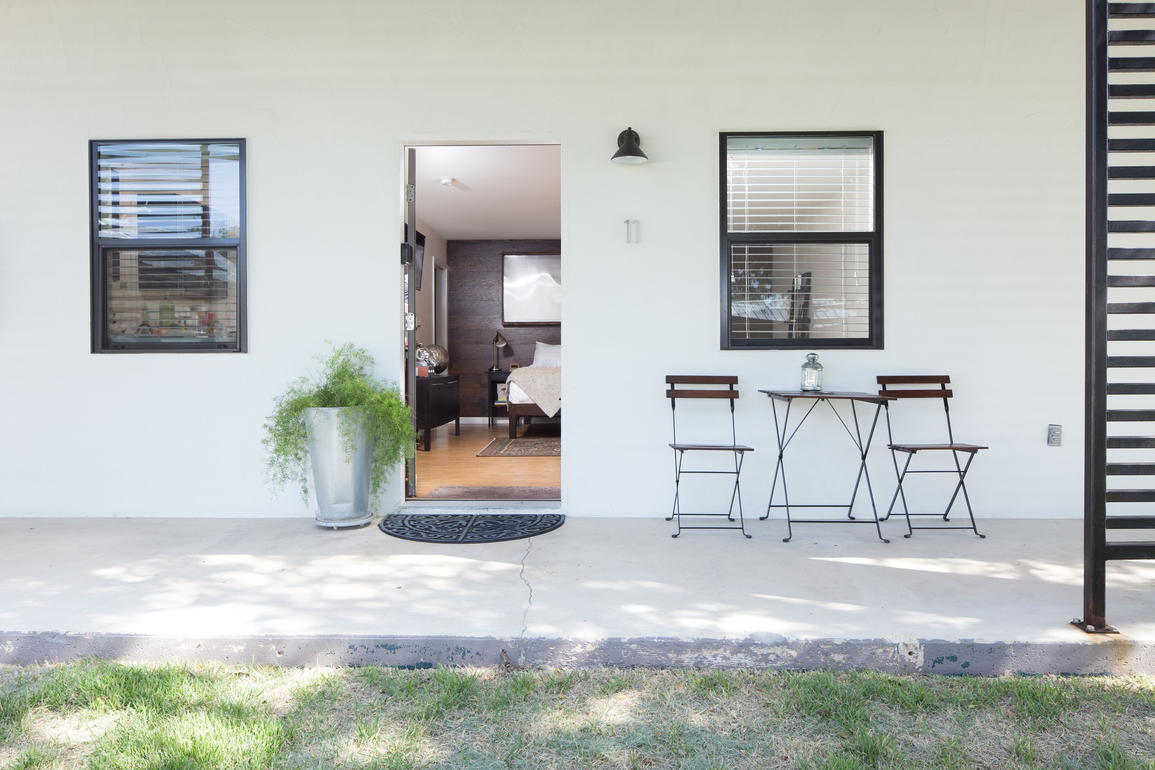 A modern house with a front door, a small patio with a table and chairs, and a potted plant.