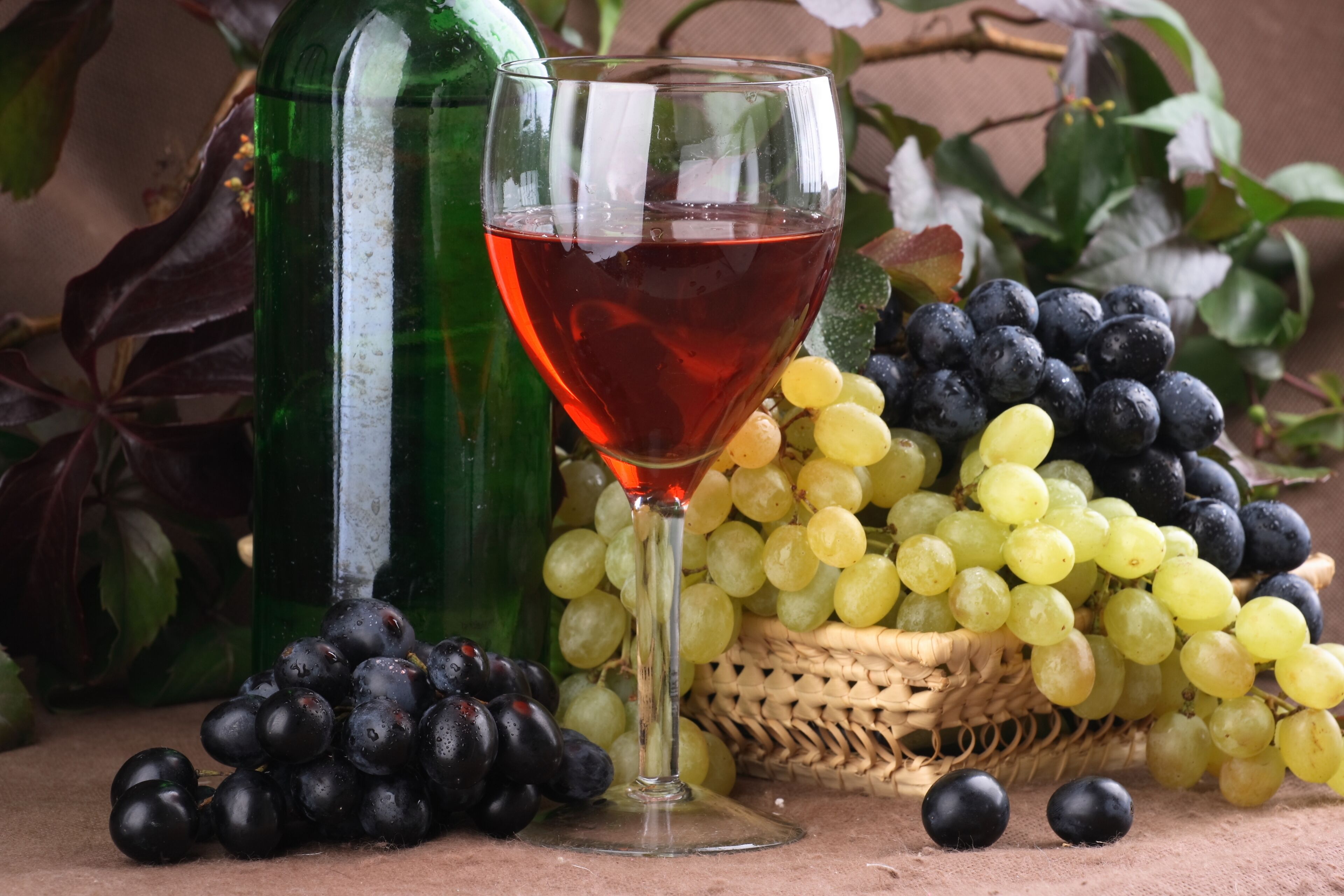 A glass of red wine, a bottle, and a basket of grapes.