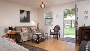 A living room with a sofa, coffee table, and chair, a dining table, and a door leading outside. - Hotel Flora & Fauna (Wimberley)
