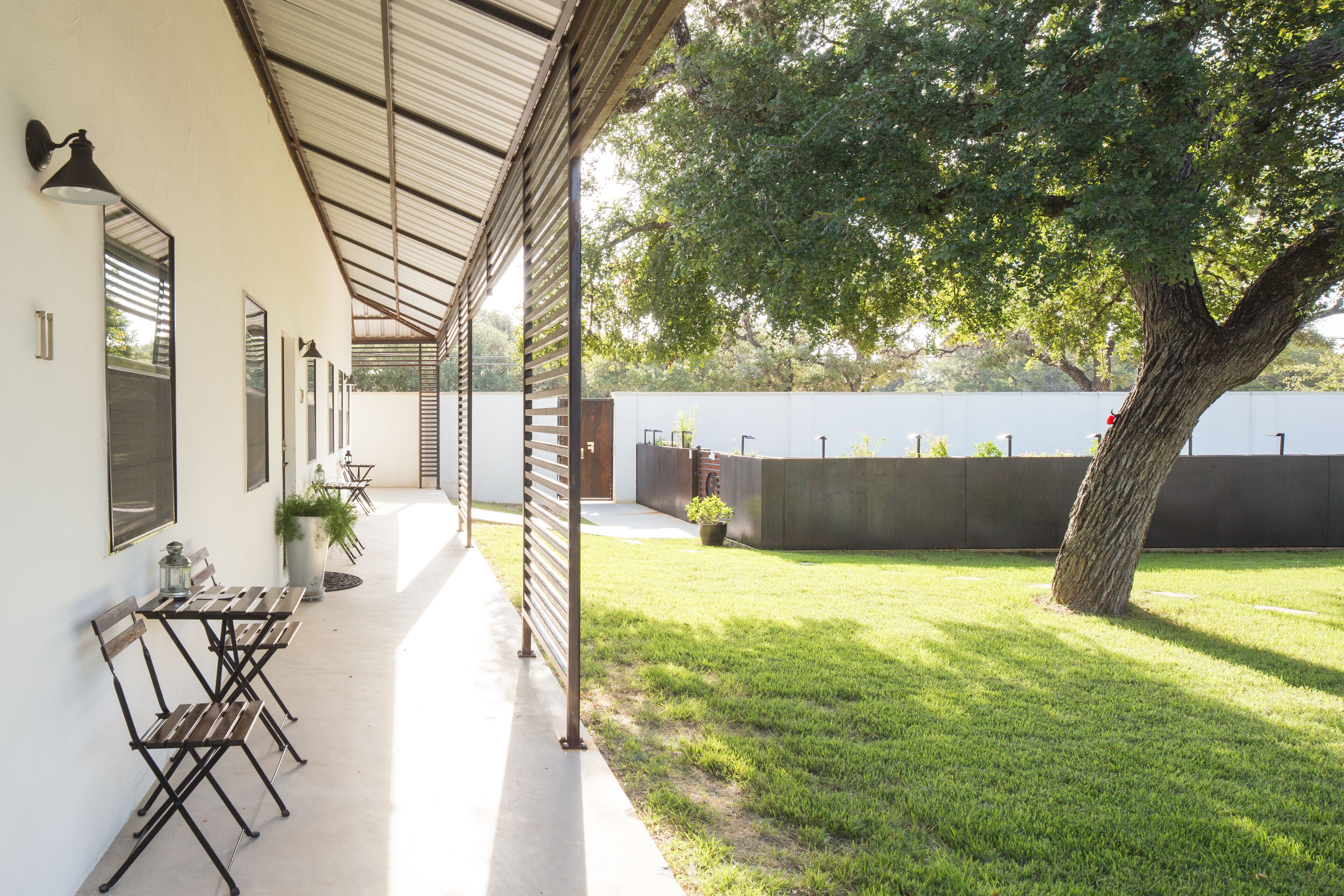 A covered patio area with outdoor seating and a large tree.