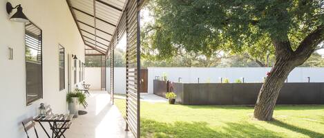 A covered patio area with outdoor seating and a large tree.