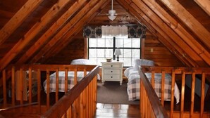 A cozy attic bedroom with wooden beams, two beds, a nightstand, and a window with curtains. - Deer Haven (Blue Ridge)