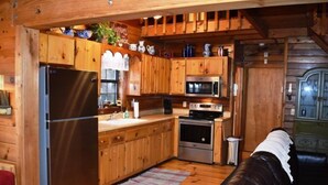 A wooden cabin-style kitchen with a refrigerator, microwave, stove, and wooden cabinets. - Deer Haven (Blue Ridge)