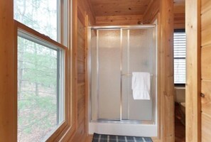Ein Badezimmer einer Holzhütte mit Duschkabine aus Glas und einem Fenster.