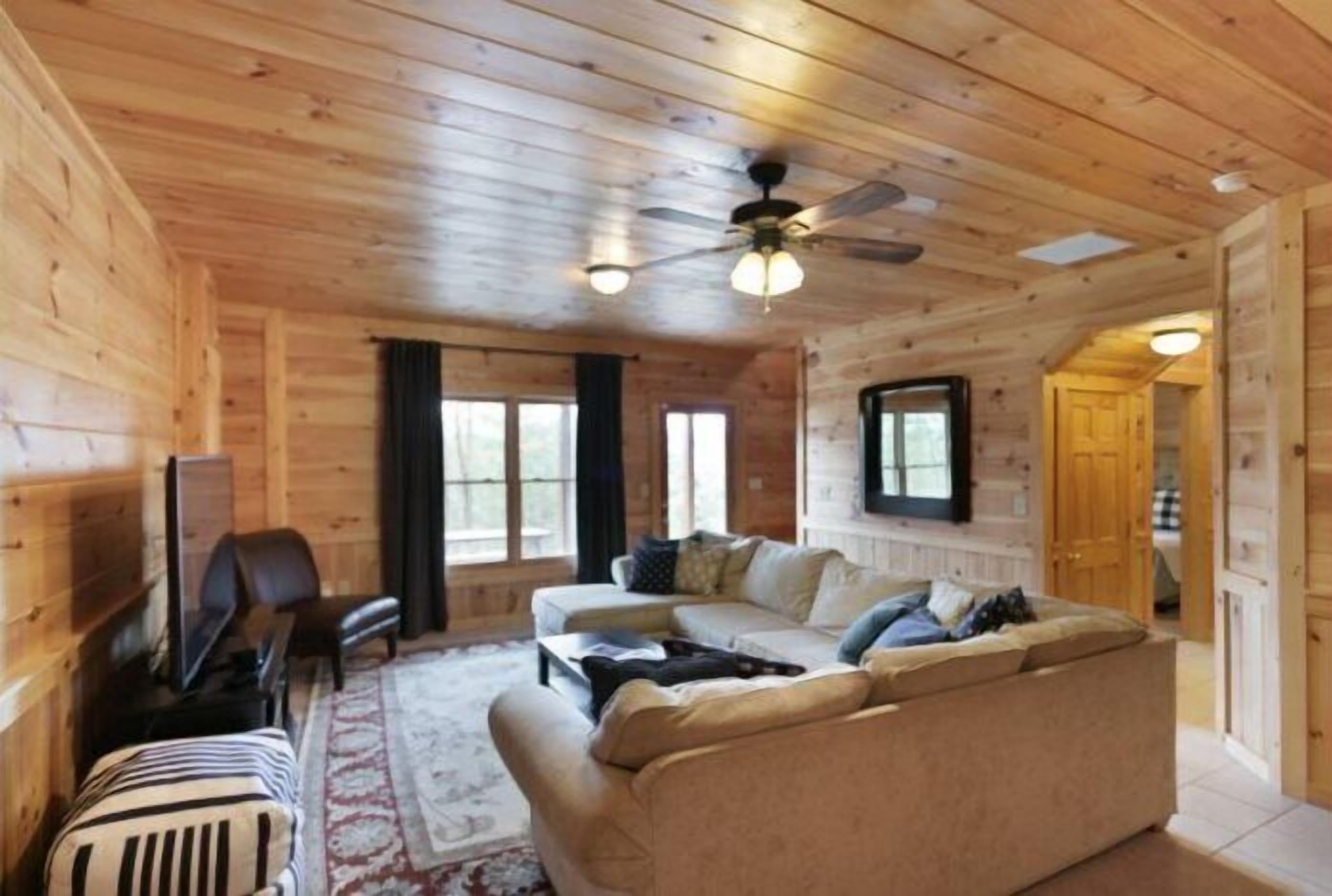 A cozy log cabin interior with a sofa, TV, and a ceiling fan.