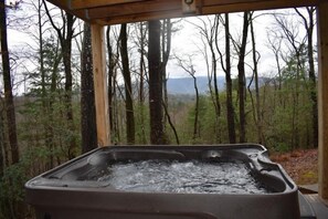 Un jacuzzi en una cabaña de madera rodeada de árboles, con vistas a la montaña.