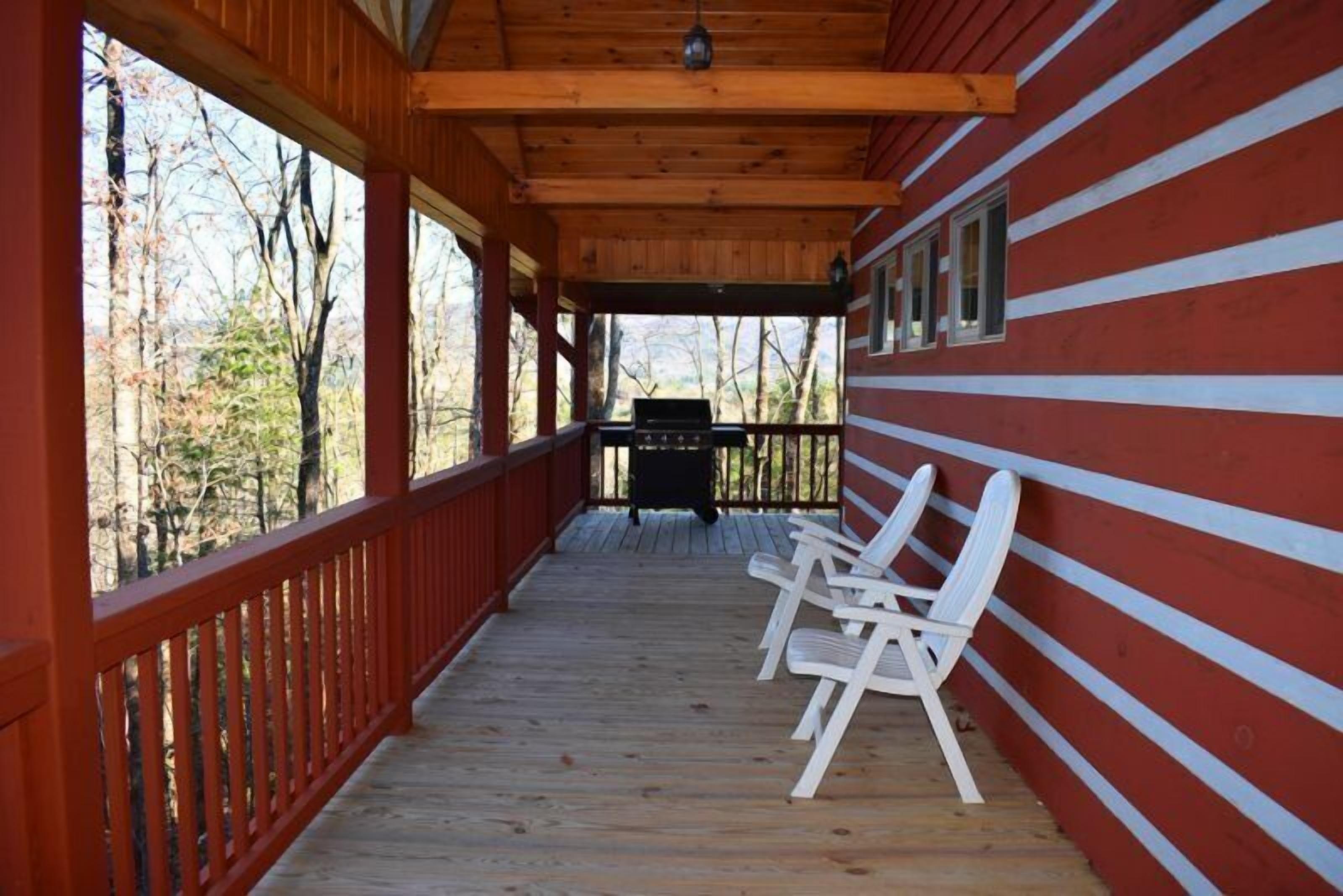 A covered porch with wooden railings, a grill, and white plastic chairs.