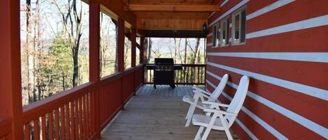 A covered porch with wooden railings, a grill, and white plastic chairs.