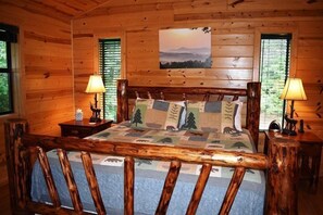 A wooden cabin bedroom with a bed, two nightstands, and a painting on the wall.