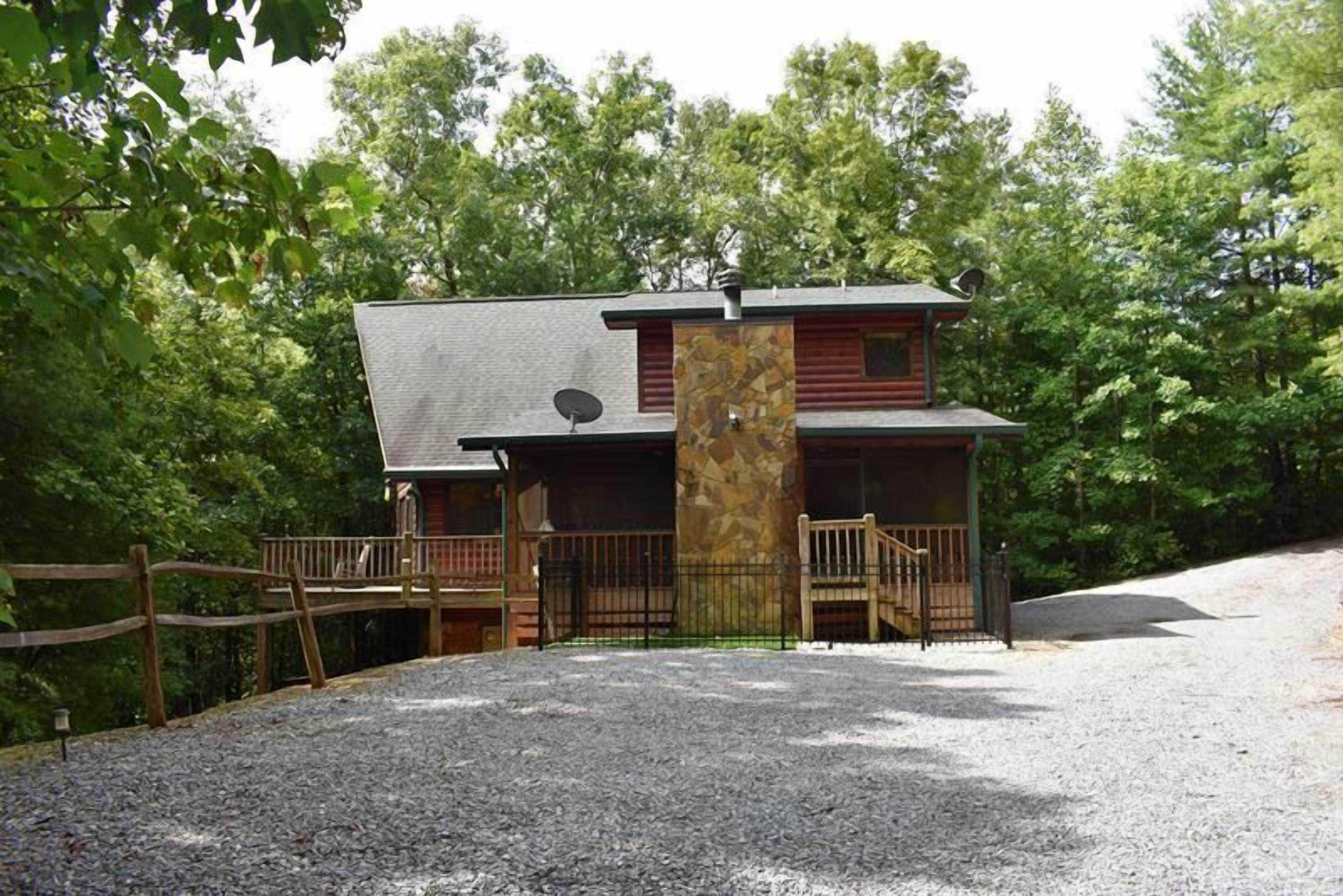A two-story cabin with a stone pillar, a deck, and a gravel driveway.