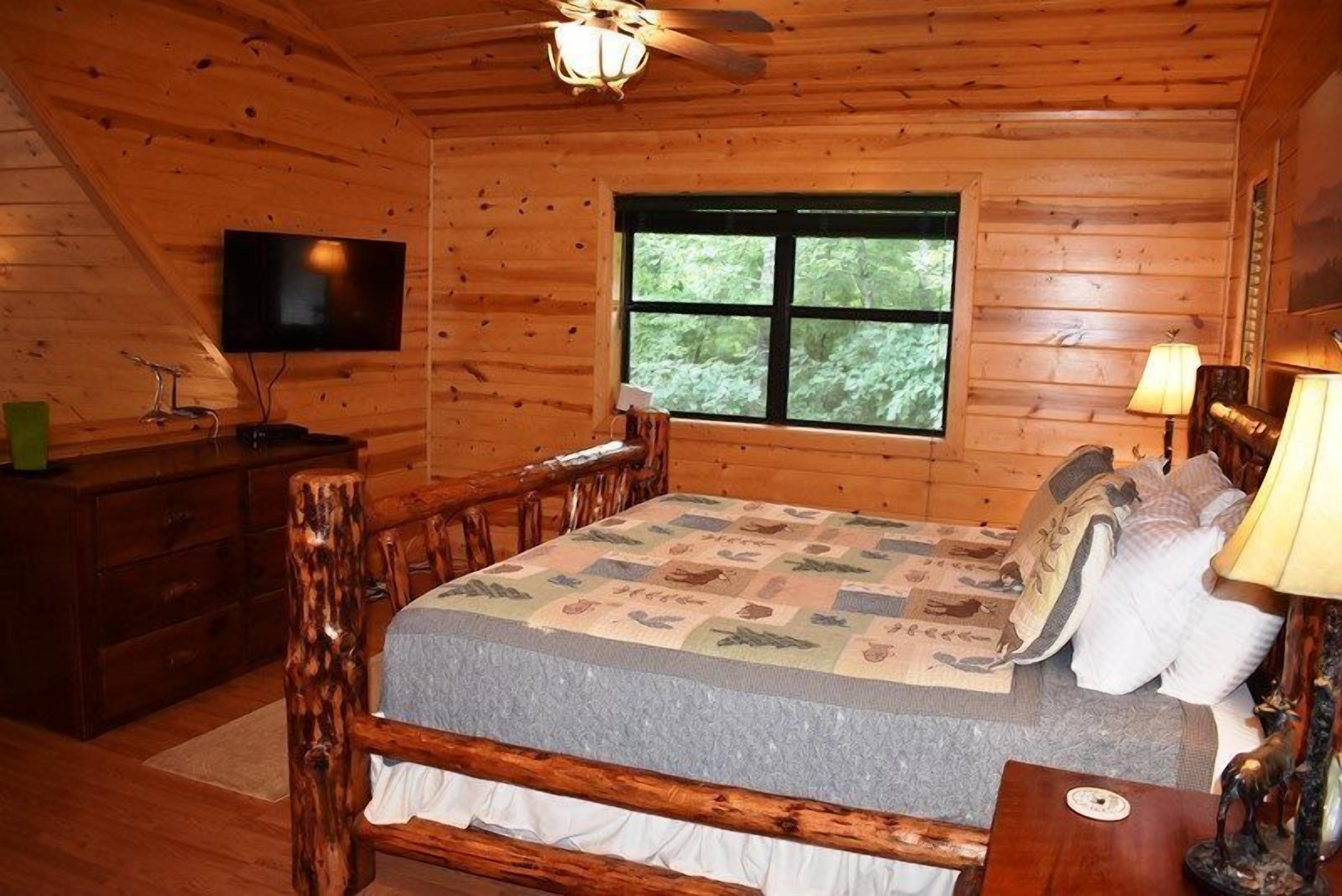 Een houten slaapkamer met een bed, een televisie, een raam en een houten dressoir.
