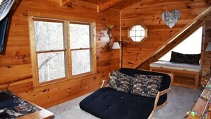 A cozy wooden cabin room with a bed, a small table, and a window. - Barefoot Lodge (Mineral Bluff)