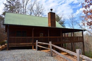 Un rustico chalet con tetto in lamiera verde, rivestimento in legno e un portico con ringhiera in legno.