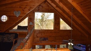 A wooden cabin with a loft bedroom, a dining area, and a large window providing a view of trees. - Barefoot Lodge (Mineral Bluff)
