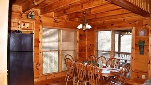 A wooden cabin interior with a dining table, chairs, a refrigerator, and a chandelier. - Barefoot Lodge (Mineral Bluff)