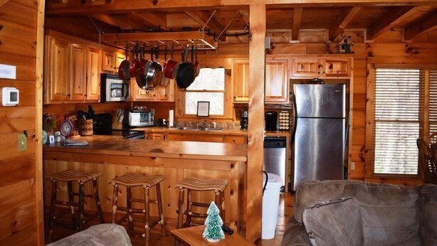 A wooden cabin interior with a kitchen, bar stools, and a couch. - Barefoot Lodge (Mineral Bluff)
