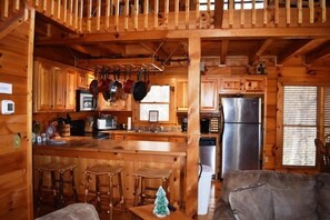 A wooden cabin interior with a kitchen, bar stools, and a couch. - Barefoot Lodge (Mineral Bluff)