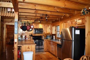 Cucina di una casetta in legno con un fornello, microonde, frigorifero e pentole appese.