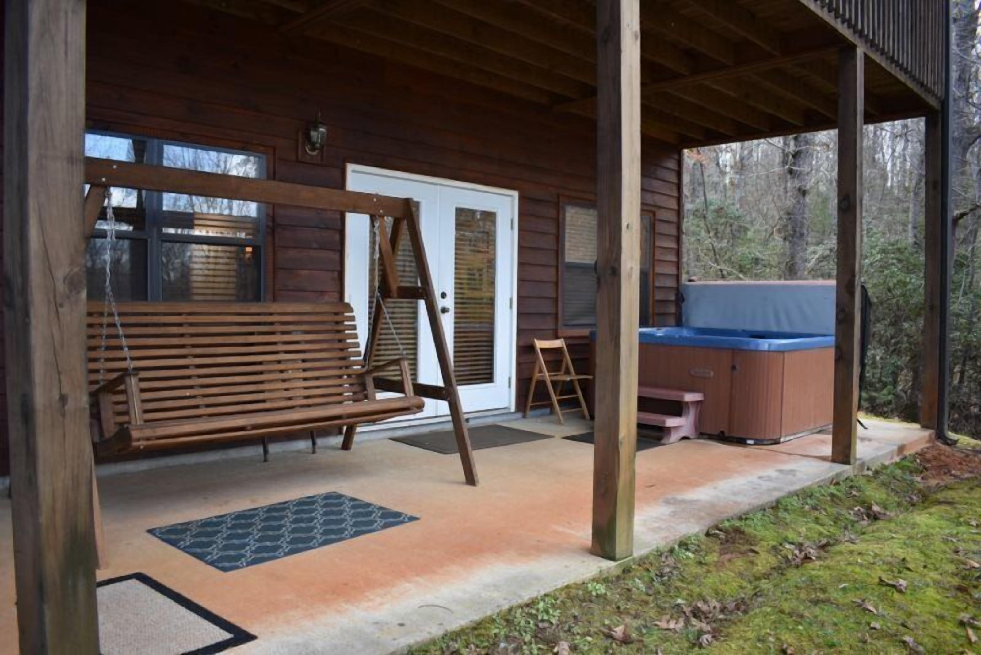 Une véranda en bois avec une balançoire, un jacuzzi et une porte.