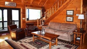 Interior acolhedor de uma cabana com escada de madeira, móveis de couro e decoração rústica.