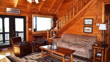 A cozy cabin interior with a wooden staircase, leather furniture, and a rustic decor.