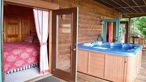 Uma cabana de madeira com uma cama, uma banheira de hidromassagem e uma porta que dá para outro quarto.