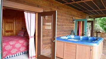 A wooden cabin with a bed, a hot tub, and a door leading to another room.