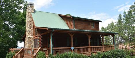 A log cabin with a stone chimney, a porch, and a covered deck.