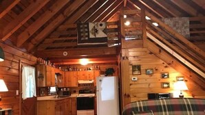 A cozy cabin interior with wooden walls, a kitchen area, a dining table, and a plaid sofa. - Serenity Summit (Blue Ridge)