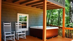 A wooden deck with a hot tub, two rocking chairs, and a window. - Serenity Summit (Blue Ridge)