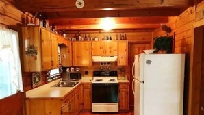 A compact kitchen with wooden cabinets, a stove, a microwave, and a refrigerator. - Serenity Summit (Blue Ridge)