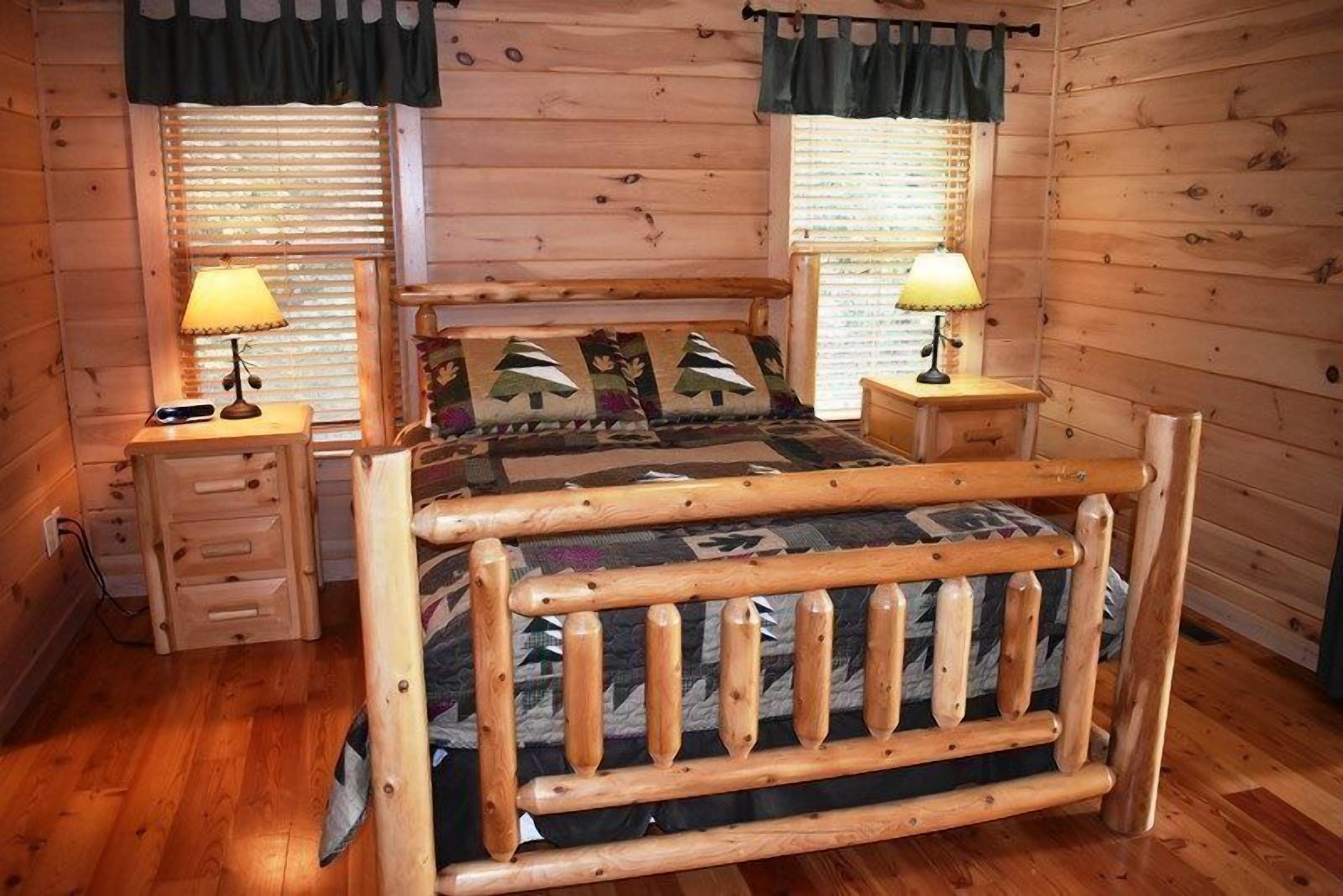 A wooden cabin bedroom with a bed, two nightstands, a lamp on each, and a window with blinds.