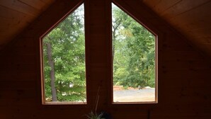 Una stanza con soffitto in legno e due finestre che danno su alberi.