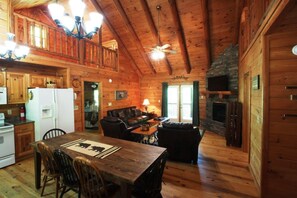 A cozy cabin interior with a dining area, a living room with a fireplace, and a kitchen with wooden cabinets and a refrigerator. - Chimney Path on Fightingtown Creek (McCaysville)