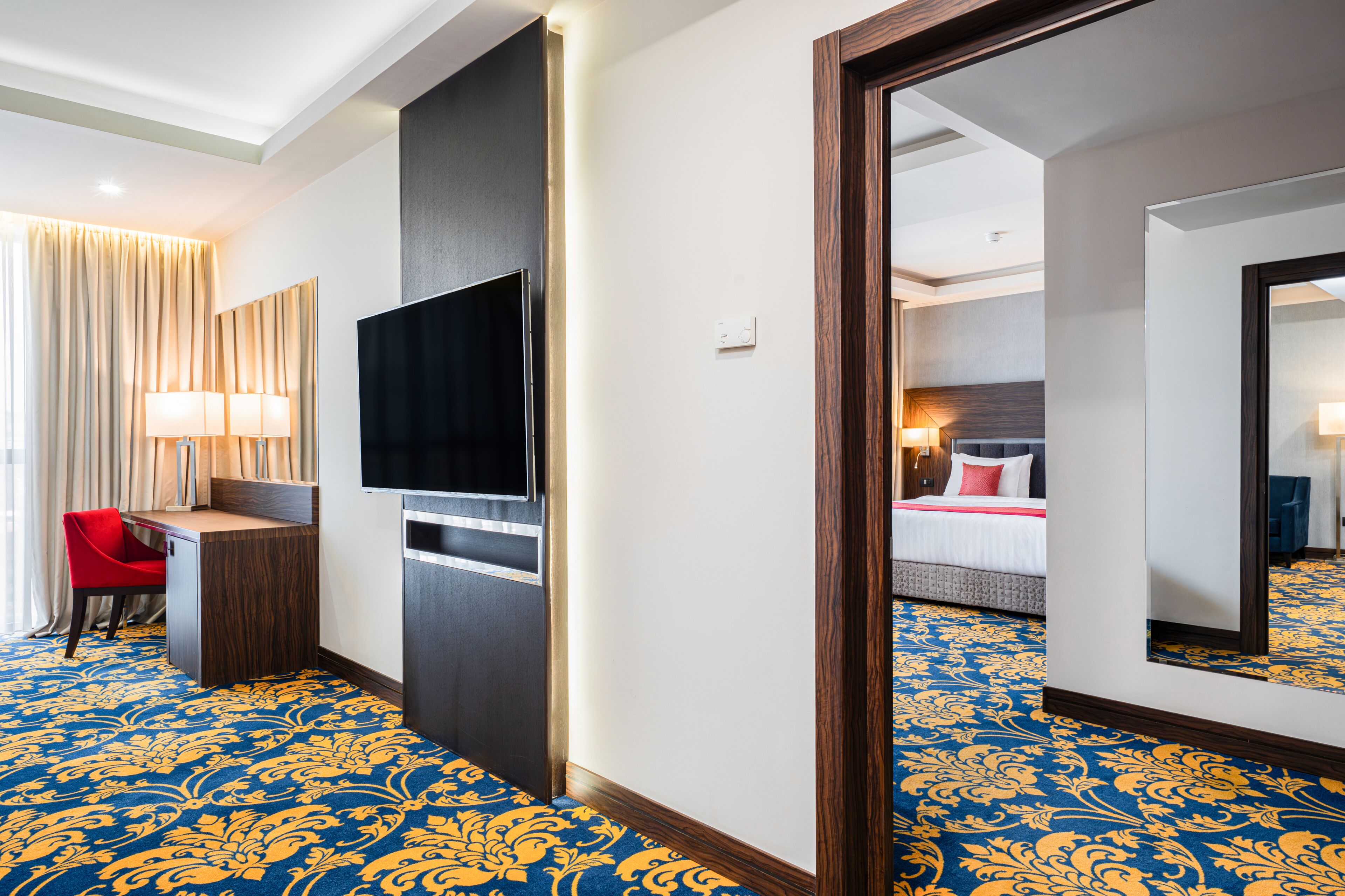 A hotel room with a large bed, a desk with a chair, a television, and a mirror.