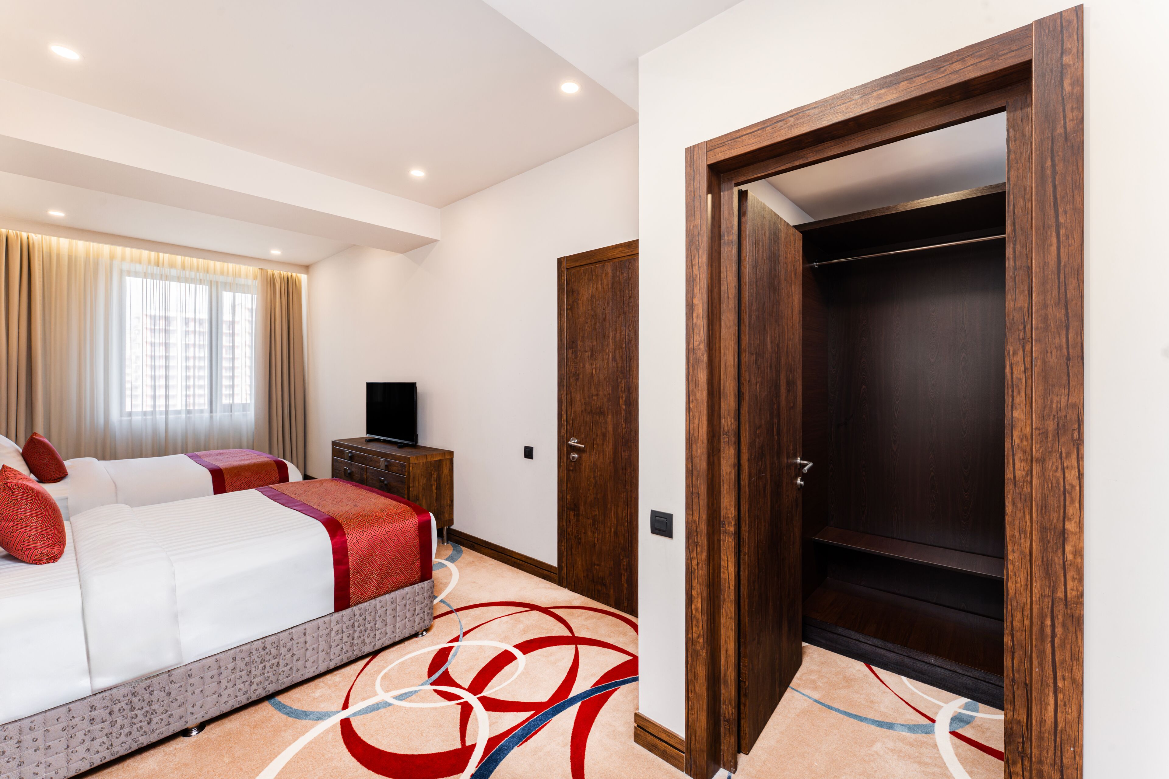 A hotel room with a bed, a television, a wardrobe, and a carpet with a geometric design.